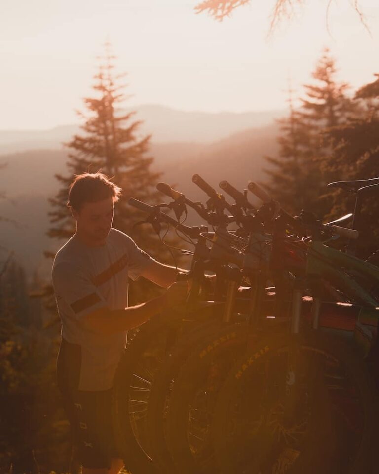 man grabbing a bike off a bike rack with sun setting behind him on the forest landscape Photo-by-Nick-Rickert-via-Unsplash-1