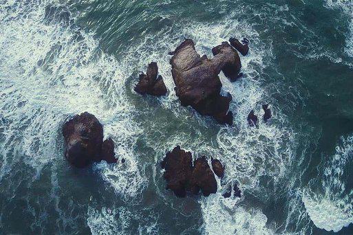 Aerial view of water crashing on rocks in the ocean.